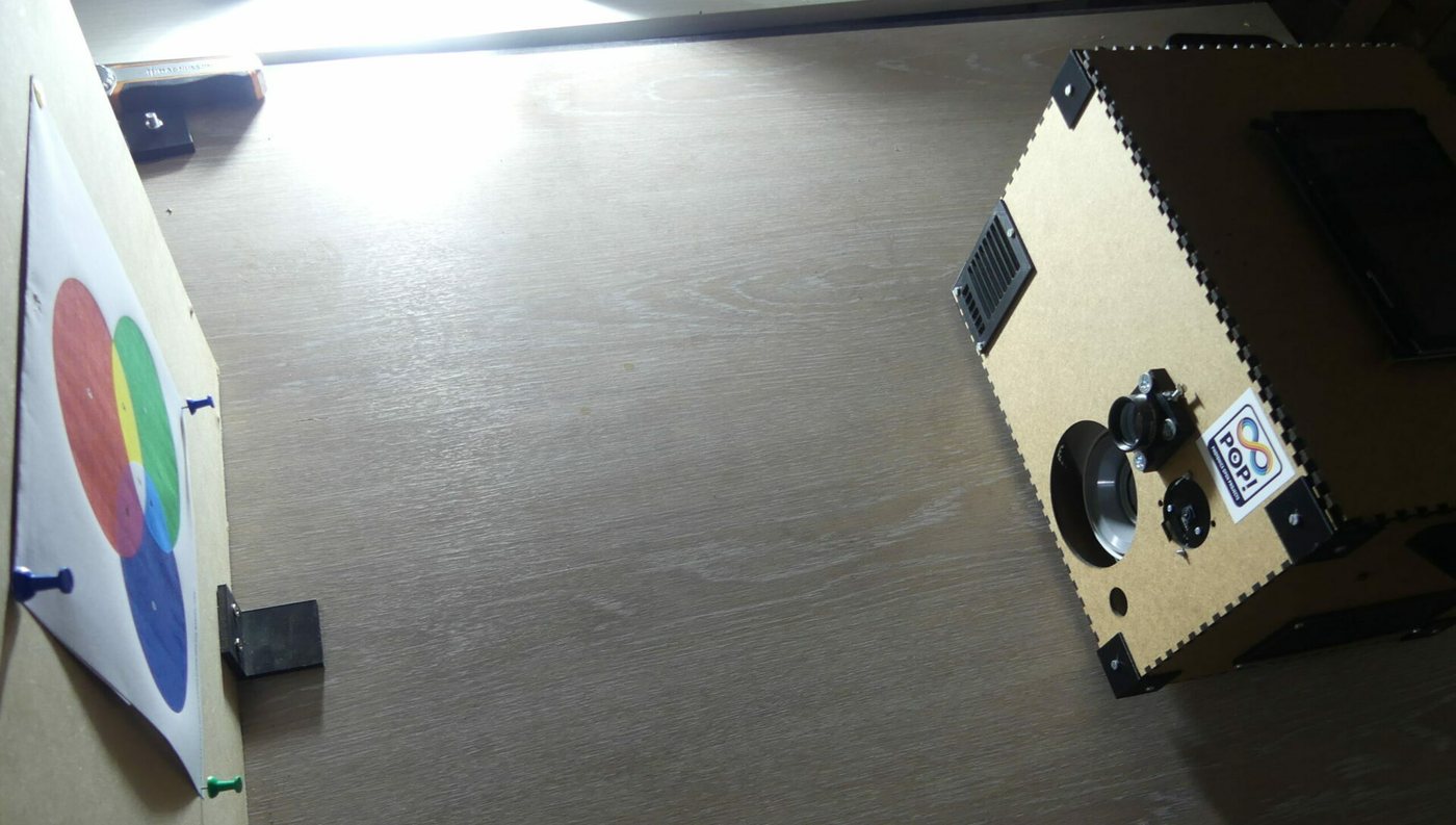 A laser-cut ONE-PIX kit prototype next to a colour-calibration target on a workbench